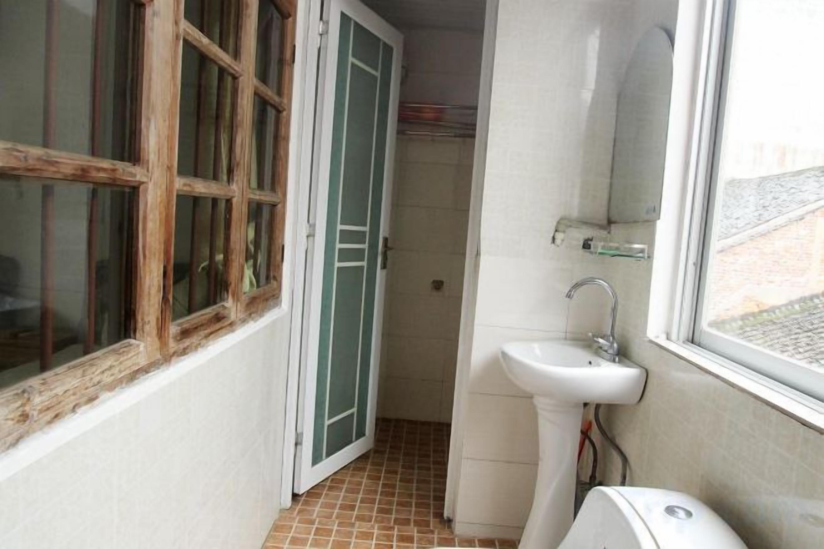 Un baño estrecho con un lavamanos blanco, una ventana y una puerta que da a otra habitación.