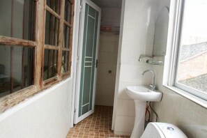 Une petite salle de bain avec un lavabo blanc, une fenêtre et une porte donnant sur une autre pièce.