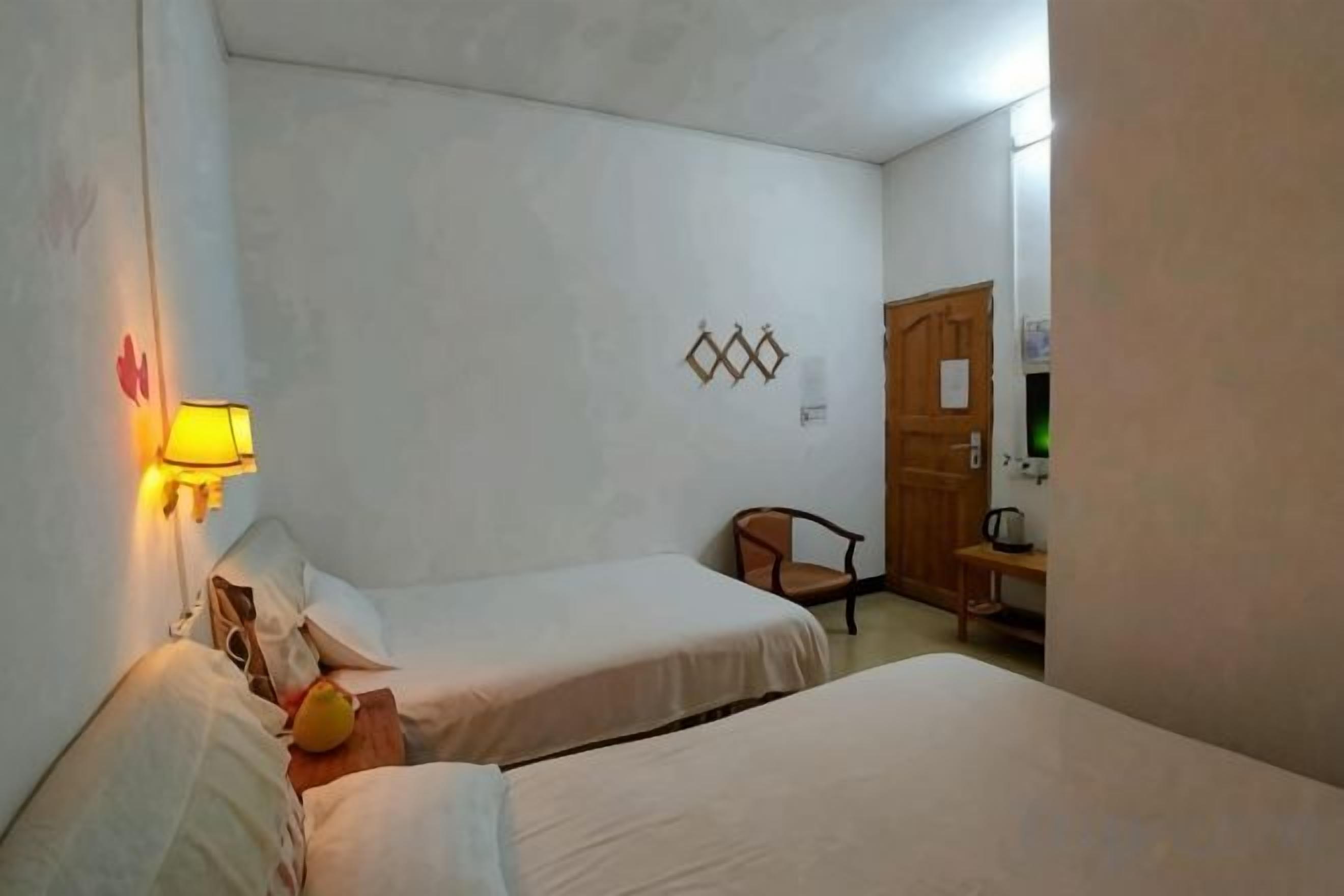 A room with two beds, a chair, a desk, and a wall-mounted lamp.
