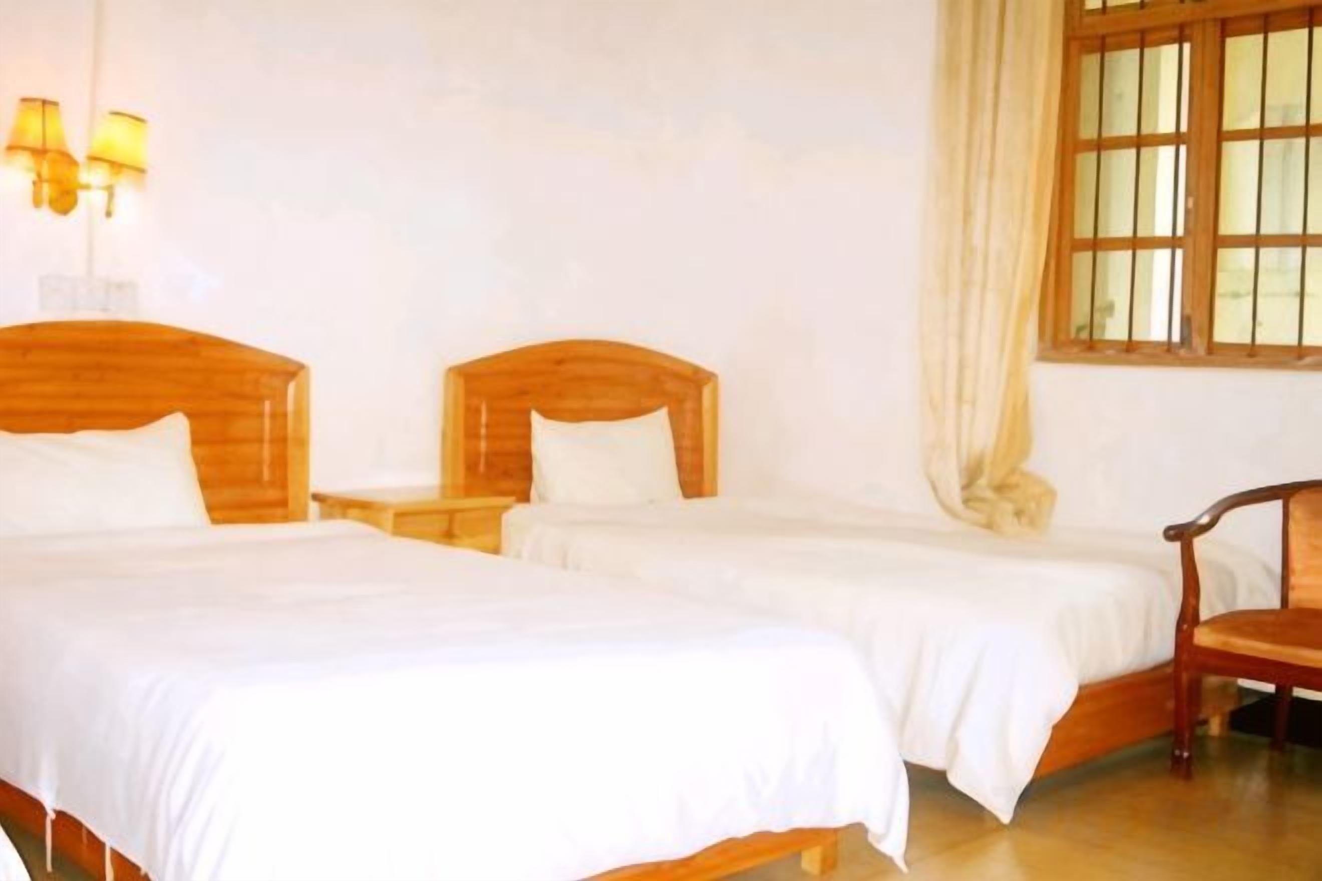 A hotel room with two wooden beds, a nightstand, a chair, and a window with curtains.