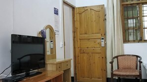 A room with a wooden desk, a television, a chair, a wooden door, and a window with curtains. - Yangshuo Culture House (Yangshuo)