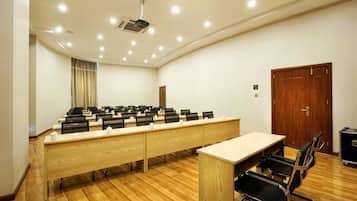 A conference room with a long table, chairs, a projector, and a wooden floor.