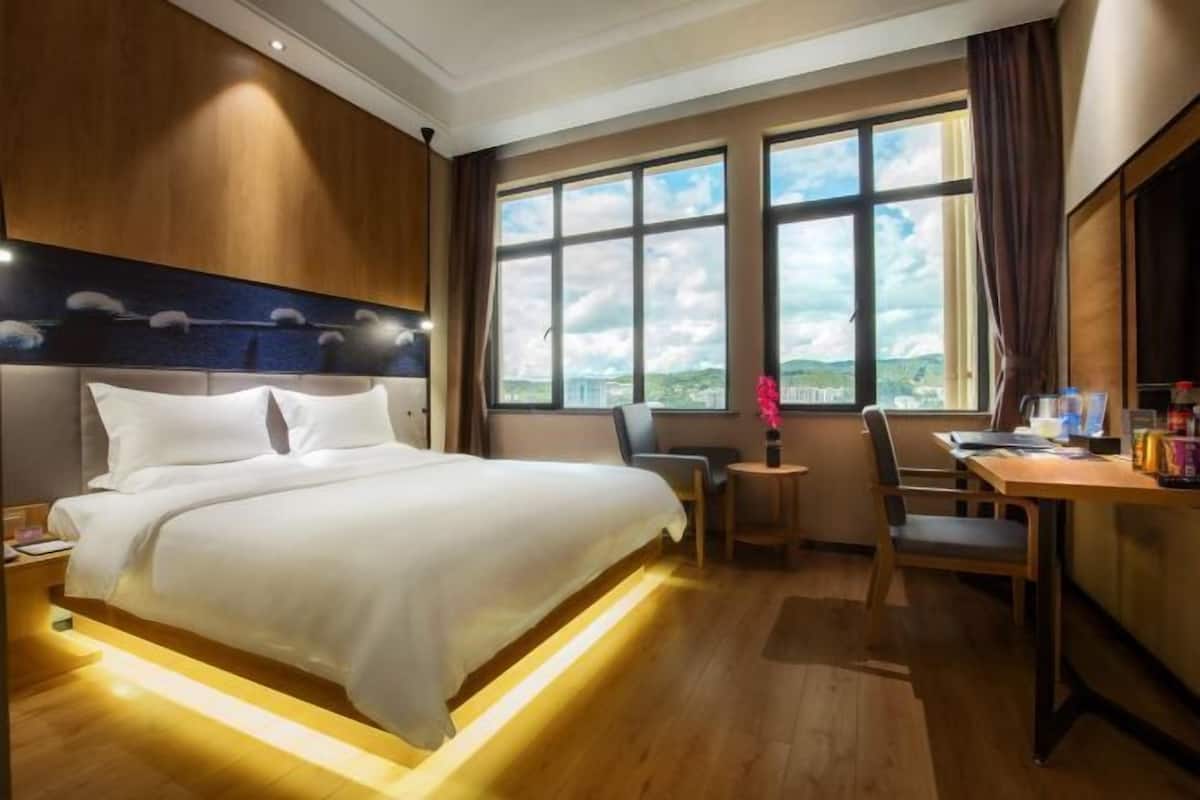 Een hotelkamer met een bed, een bureau, een stoel en grote ramen met uitzicht.
