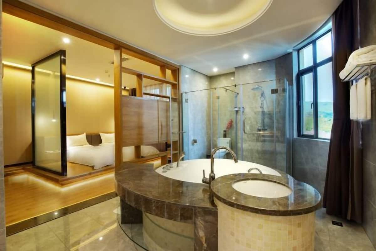 Een moderne badkamer met een grote marmeren wastafel, een douche met glazen wanden, en een slaapkamer met een bed en uitzicht.