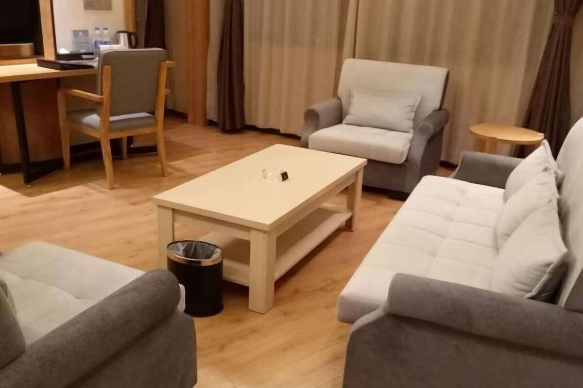 Een hotelkamer met een bank, fauteuil, klein tafeltje en een bureau met stoel.