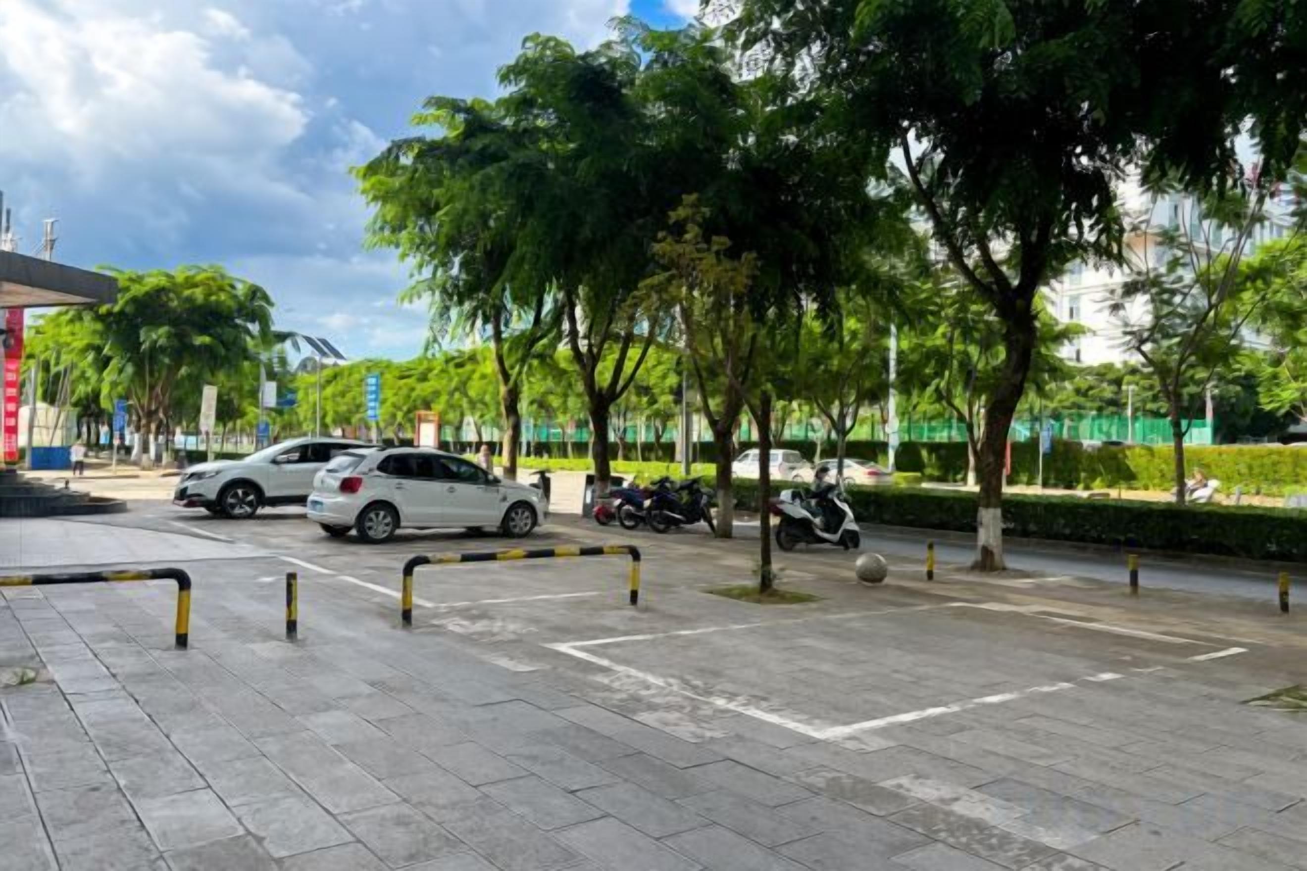 A parking area with cars and trees, a clear sky, and a building in the background.