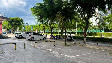 A parking area with cars and trees, a clear sky, and a building in the background.