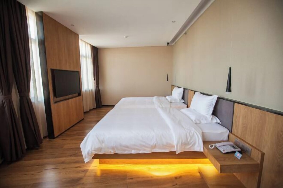 Una habitación de hotel moderna con una cama grande, una mesita de noche con teléfono y un televisor montado en la pared.