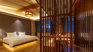 A bedroom with a bed, wooden floor, and a view of the outside.