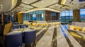 A modern hotel lobby with a curved reception desk, seating area, and large windows offering a city view.