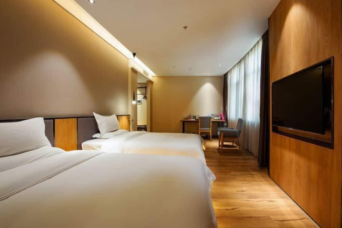 Een hotelkamer met twee bedden, een bureau, een stoel en een aan de muur bevestigde televisie.