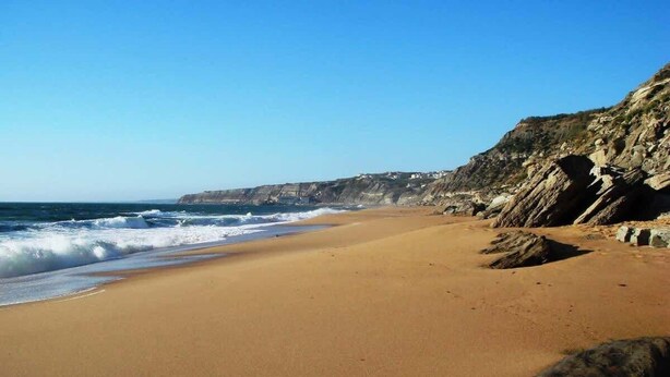Una playa con un acantilado rocoso y olas del océano.
