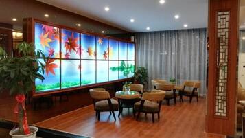 A hotel lobby with a traditional Japanese-style reception desk, a seating area with wicker chairs, and a decorative wall with a nature-themed design.