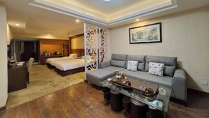 Una habitación de hotel con sofá, una mesa de centro de vidrio, cama, escritorio y un separador decorativo.
