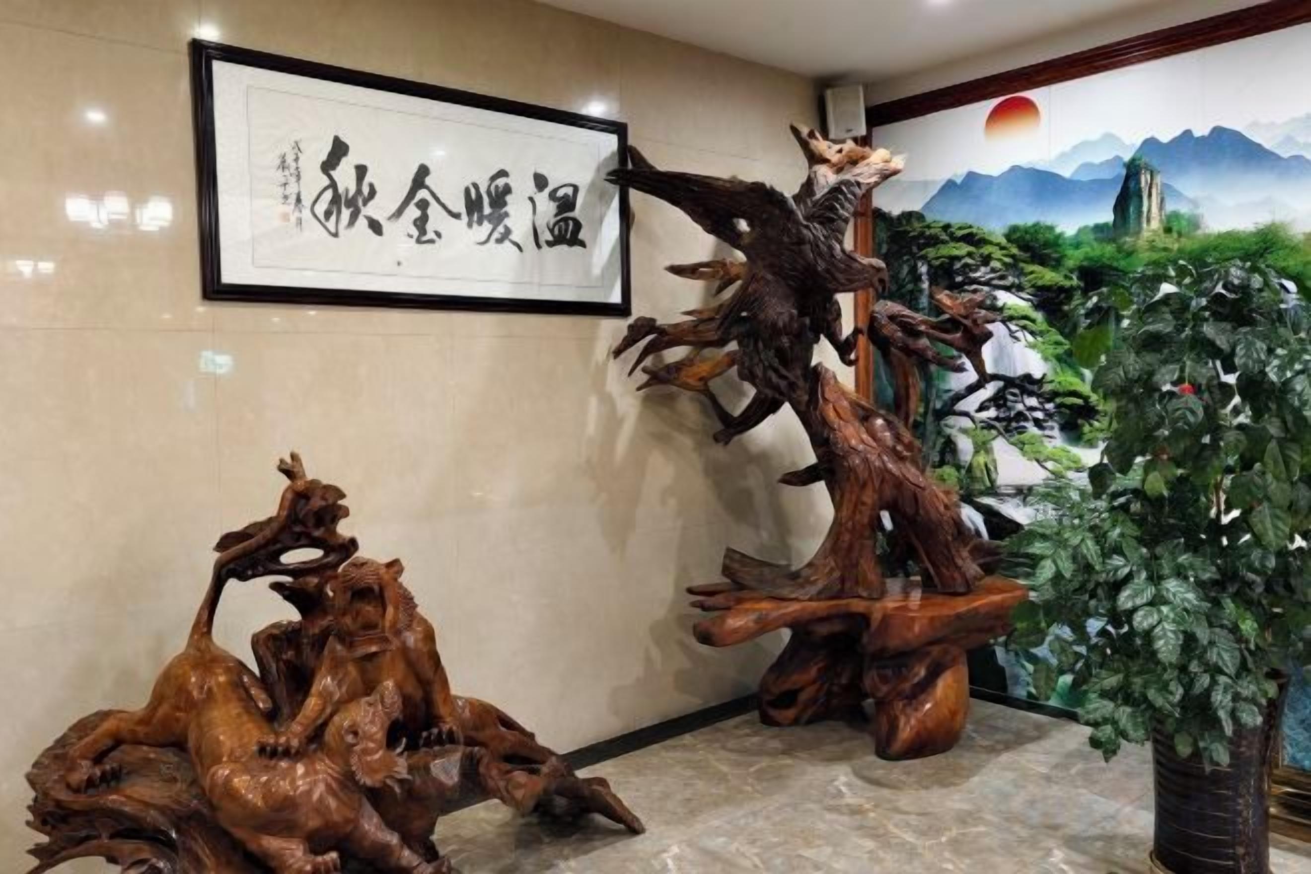 A lobby with a framed artwork, two wooden sculptures, and a large potted plant.