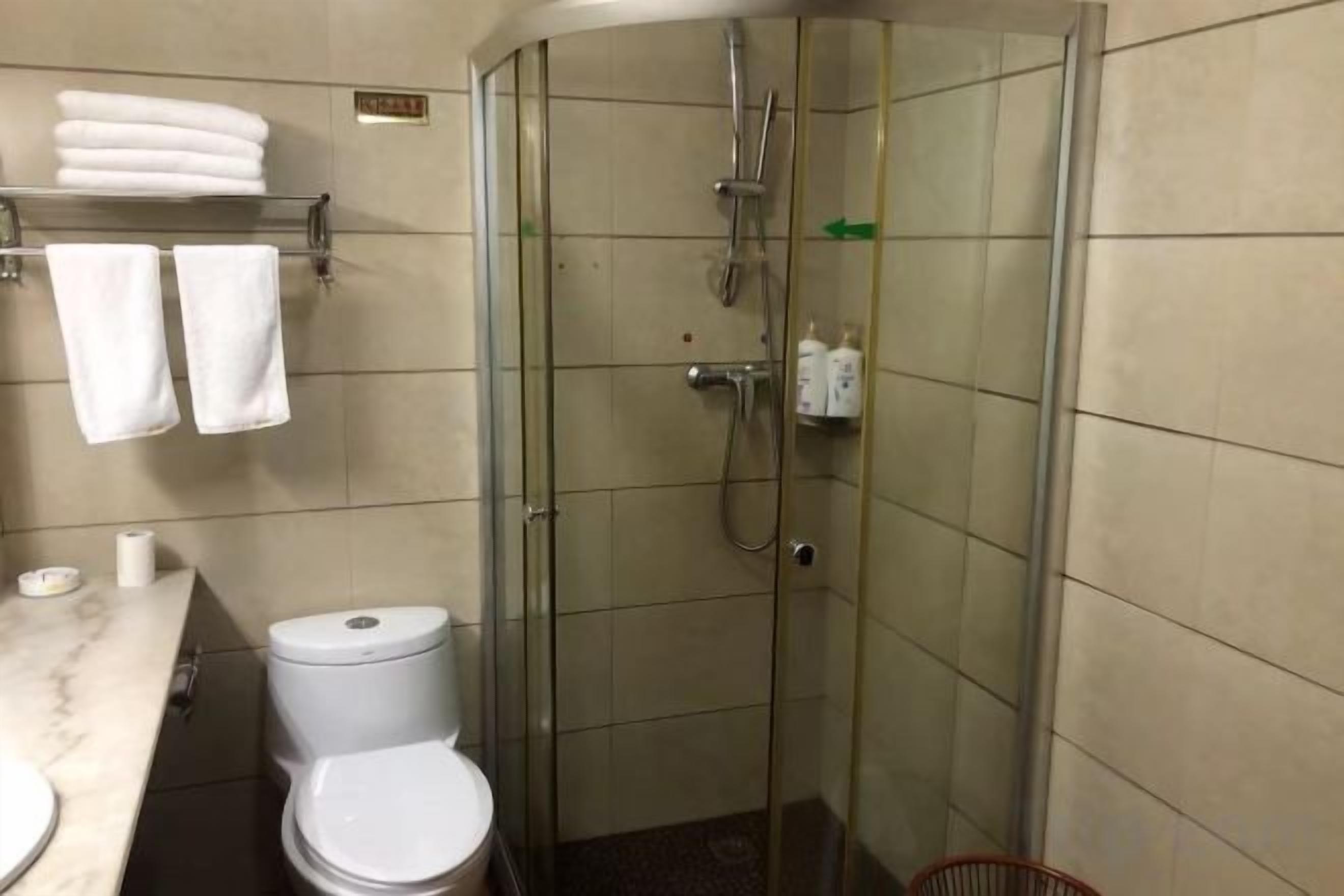 A glass-enclosed shower stall with a toilet and a marble countertop to the left.