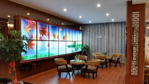 Un vestíbulo de hotel con piso de madera, un amplio biombo decorativo con diseño floral, sillas de mimbre y una pequeña mesa redonda.