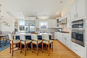 Une cuisine moderne avec des meubles blancs, des appareils en acier inoxydable et un îlot central doté de chaises.