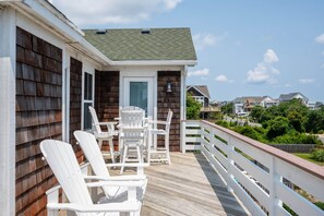 Une terrasse en bois avec des chaises blanches et une table, donnant sur un quartier résidentiel.