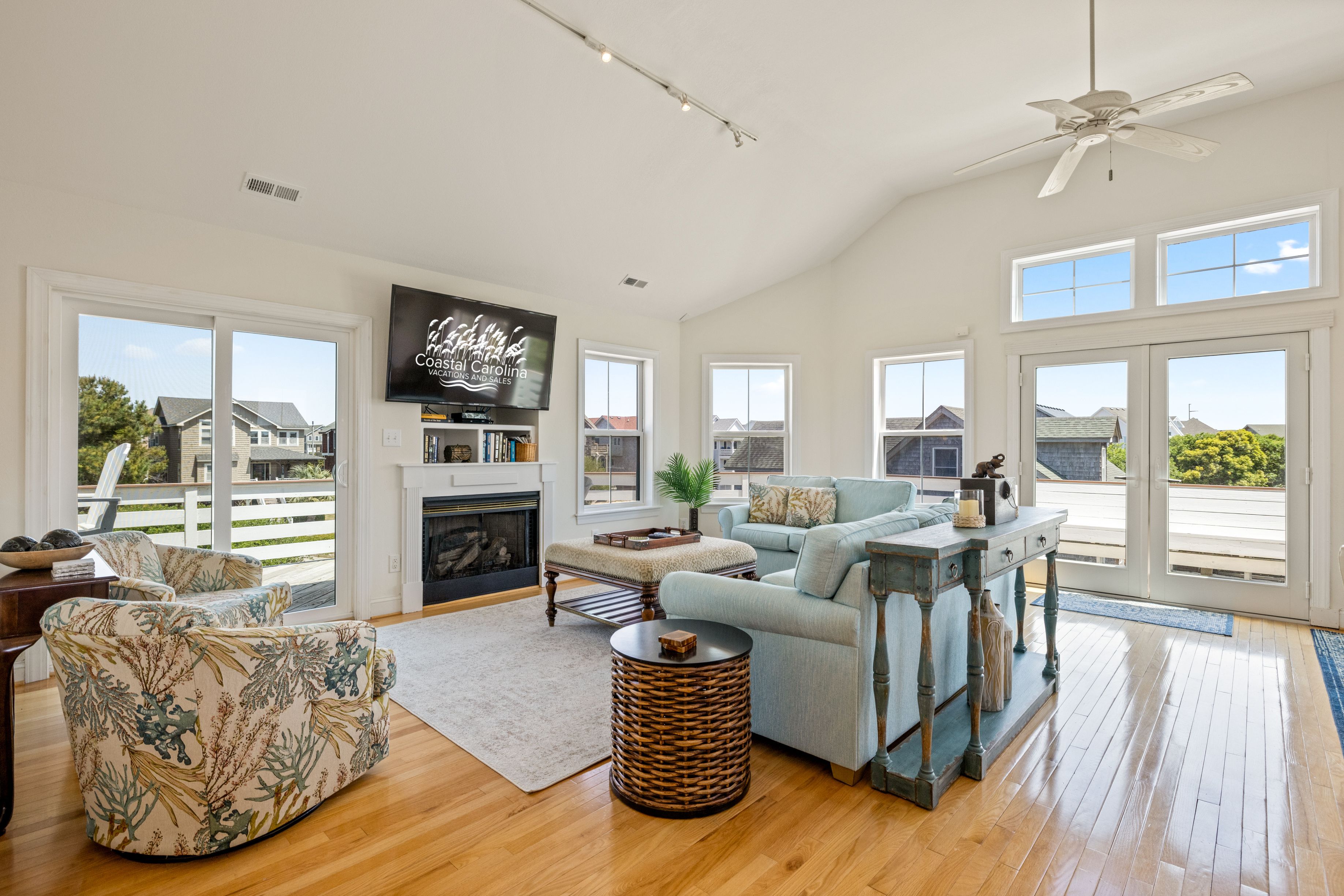 A spacious living room with a fireplace, large windows, and a ceiling fan.