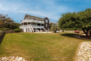 A two-story house with a balcony, a well-maintained lawn, and a wooden fence. - Salty Cs: Stunning Oceanside Home with Private Pool, Hot Tub and Pool Table! (Nags Head)