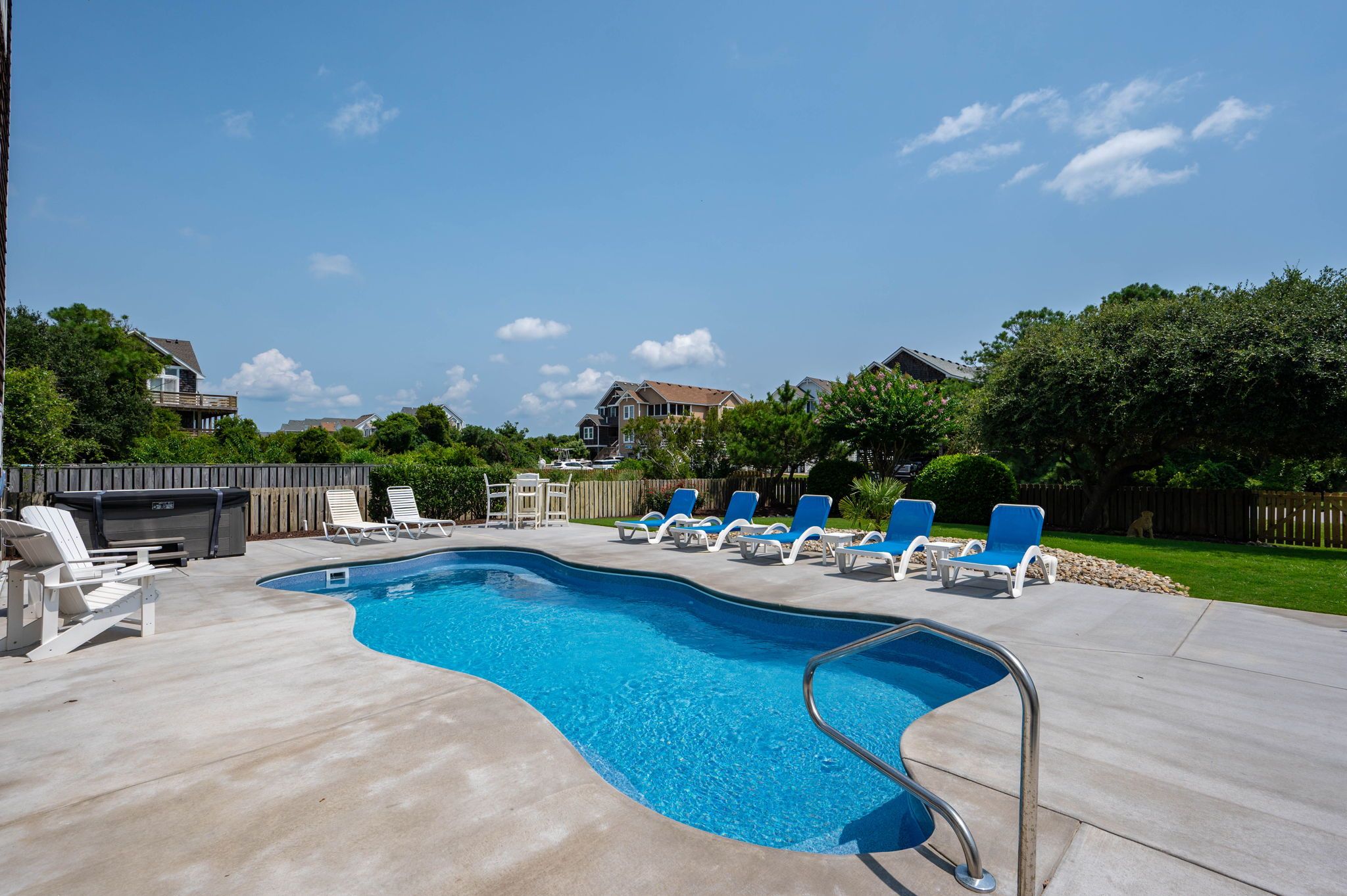 A swimming pool with a concrete deck, surrounded by lounge chairs and a wooden fence.