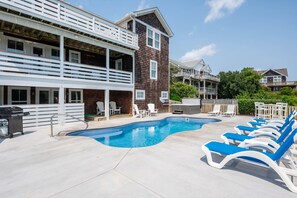A swimming pool with lounge chairs, a barbecue grill, and a multi-story building with balconies.