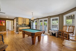 Een ruime woonkamer met een pooltafel, houten kasten en een eethoek met stoelen en een tafel.