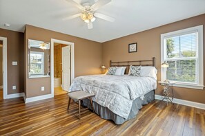 A bedroom with a bed, a ceiling fan, a window, and a door.
