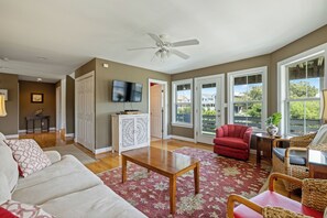 Amplia sala de estar con ventilador de techo, un sillón rojo, una mesa de centro de madera y un ventanal con vistas al exterior.