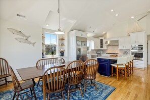 A spacious kitchen with white cabinets, a blue island, and wooden chairs. - Salty Cs: Stunning Oceanside Home with Private Pool, Hot Tub and Pool Table! (Nags Head)