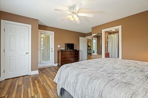 Une chambre à coucher avec un grand lit, un ventilateur de plafond, une commode et une porte donnant sur une autre pièce.