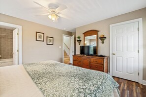 Un dormitorio con cama, cómoda, televisor y ventilador de techo.