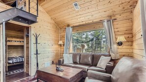Een gezellig blokhutinterieur met houten details, een bank, een salontafel en een stapelbed.