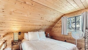 Een knus houten slaapkamer met een bed, nachtkastje en een raam met gordijnen.