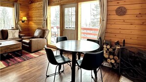 Een gezellig blokhutinterieur met houten inrichting, een ronde eettafel, lederen stoelen, een bank en een open haard.