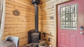 L’intérieur d’une cabane avec un poêle à bois, une porte rouge et une fenêtre avec des barreaux.