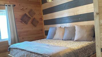 Een houten kamer met een bed, hangende lampen en een raam met gordijnen.