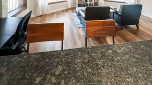 A spacious living room with a wooden floor, a black dining table, and blue chairs. - Lakefront in Duck Creek with Private Dock, 2 Units (Afton)