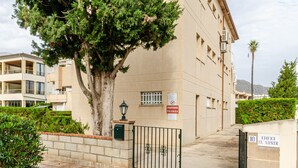 A building with a large tree in front, a gated entrance, and a sign indicating a private area. - Yourhouse El Xiprer (Pollensa)