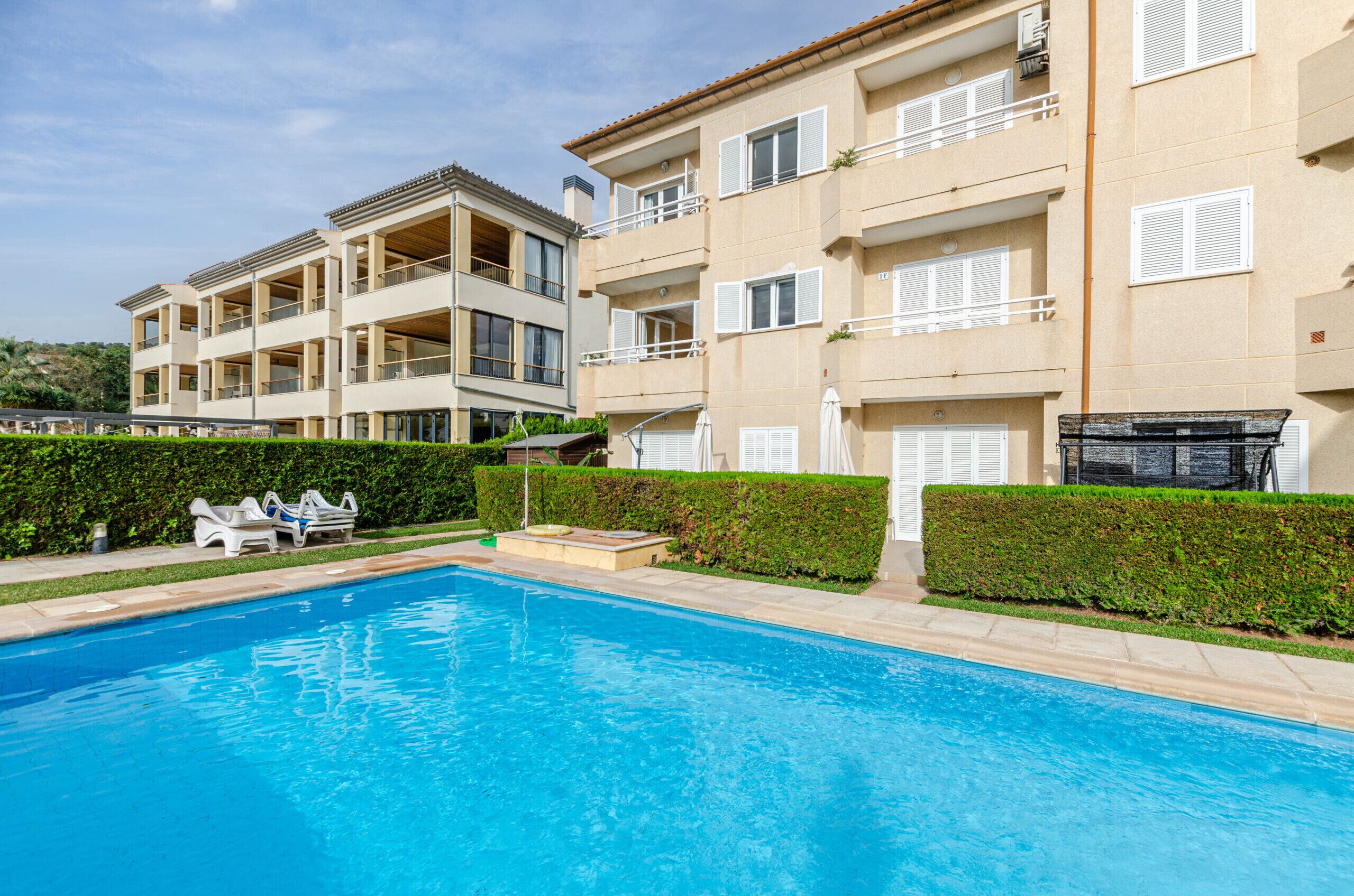 Une piscine avec des chaises longues et un bâtiment doté de balcons et de fenêtres.