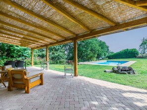Une terrasse couverte avec un sol en briques, des meubles en bois et une vue sur une piscine.