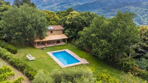 Une maison en pierre avec une piscine, entourée d’une végétation luxuriante et avec des montagnes en toile de fond.