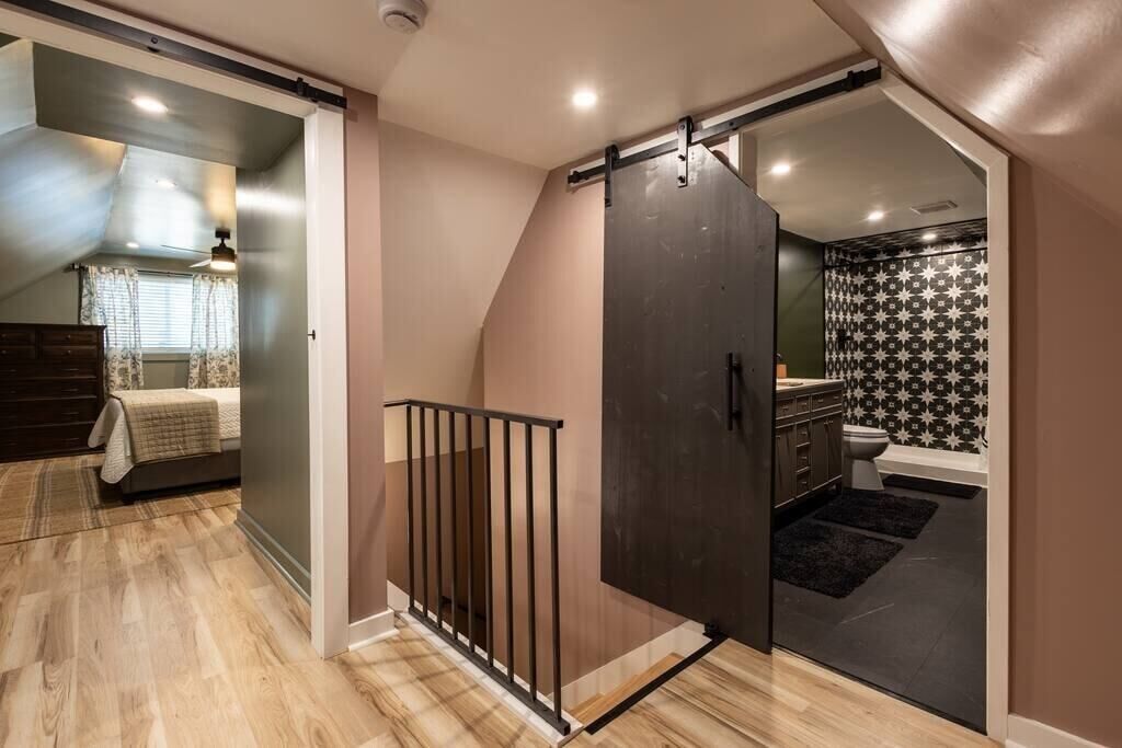 Un intérieur moderne avec un plancher en bois, une porte coulissante donnant sur une salle de bain et un lit doté d’une tête de lit.