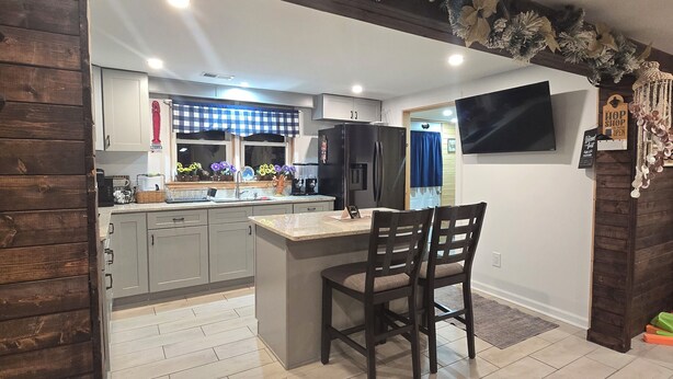 A modern kitchen with a central island, grey cabinets, and a flat-screen TV mounted on the wall. - Vacation home near the beaches!. (Pocomoke City)