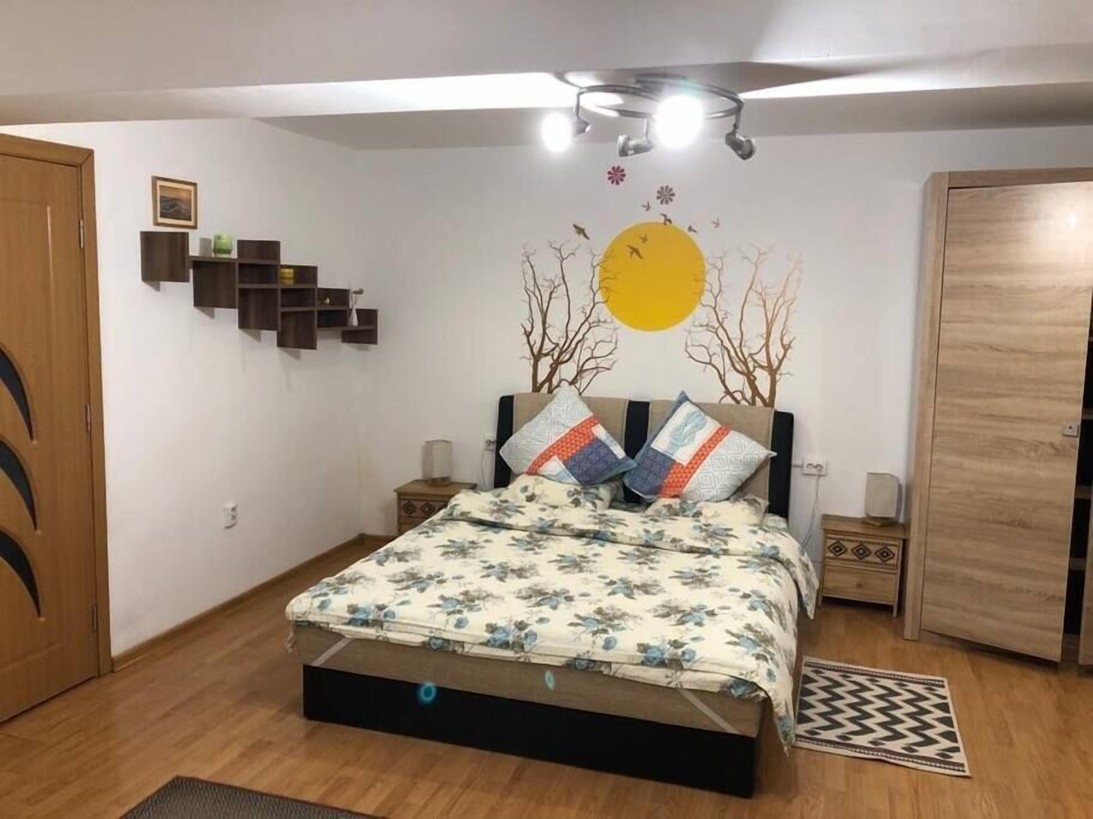 A bedroom with a bed, bedside tables, a wardrobe, a wall-mounted shelf, and a ceiling light fixture.