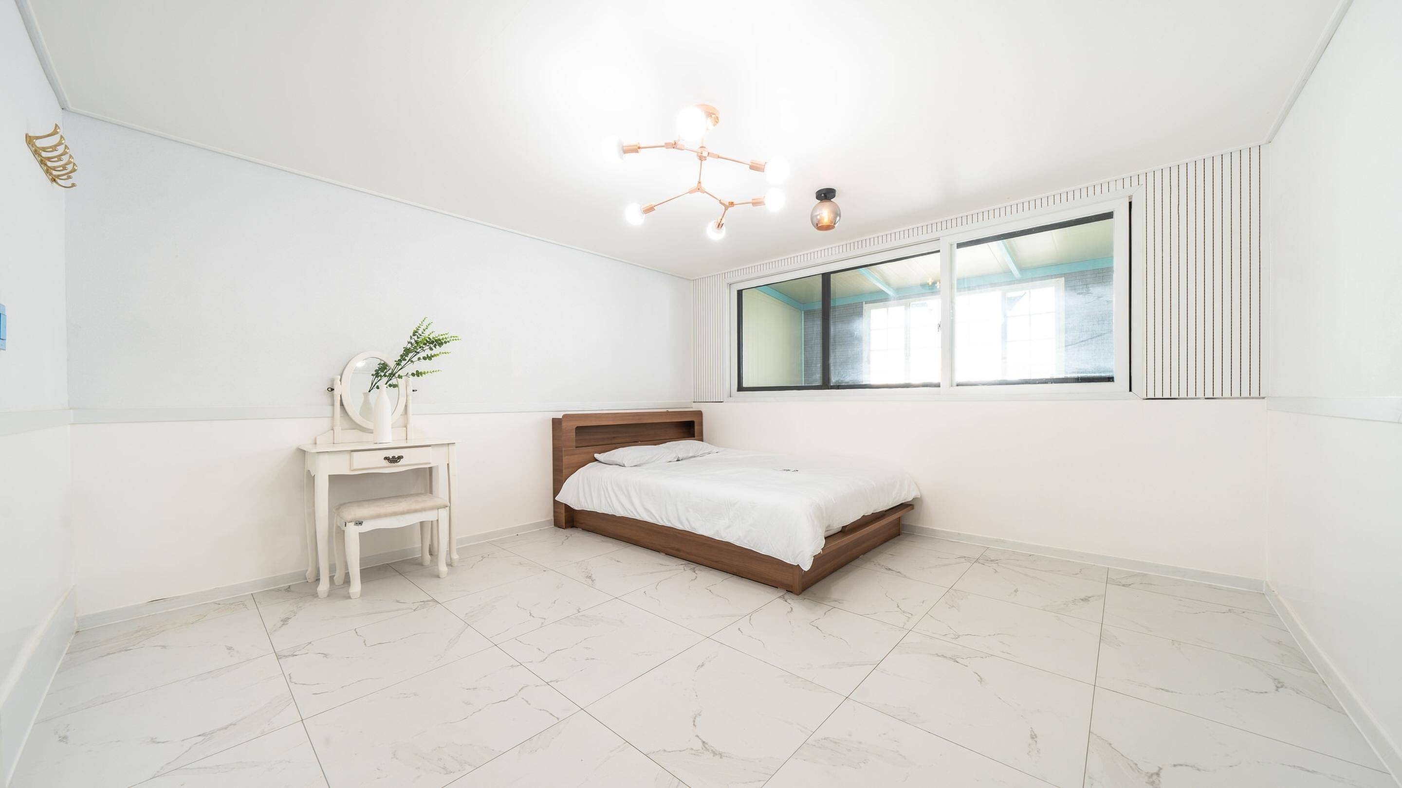 Un dormitorio con cama, tocador con espejo, ventana y lámpara en el techo.