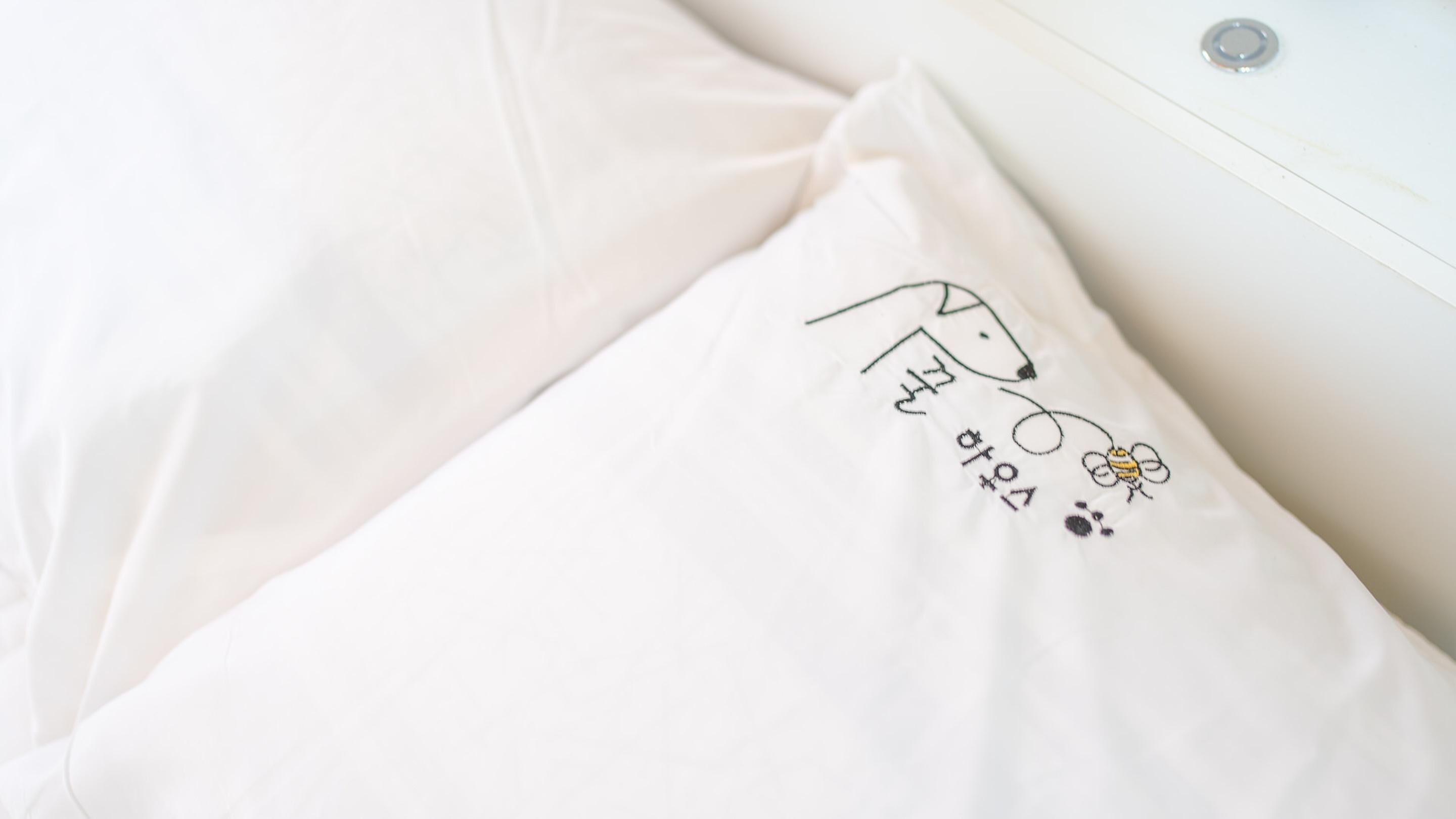A white pillow with a simple line drawing of a dog and a bee.