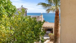 A coastal view with a palm tree, a thatched-roof structure, and a clear blue sky.