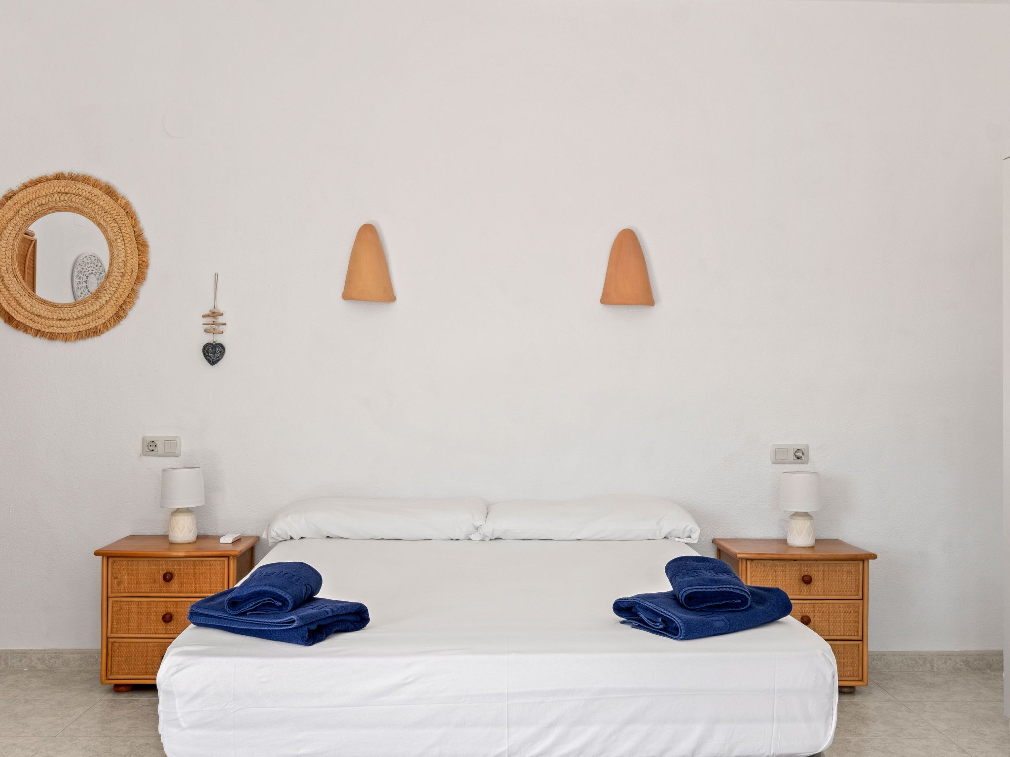 Une chambre à coucher comprenant un lit, deux tables de chevet, un miroir fixé au mur et deux appliques murales.